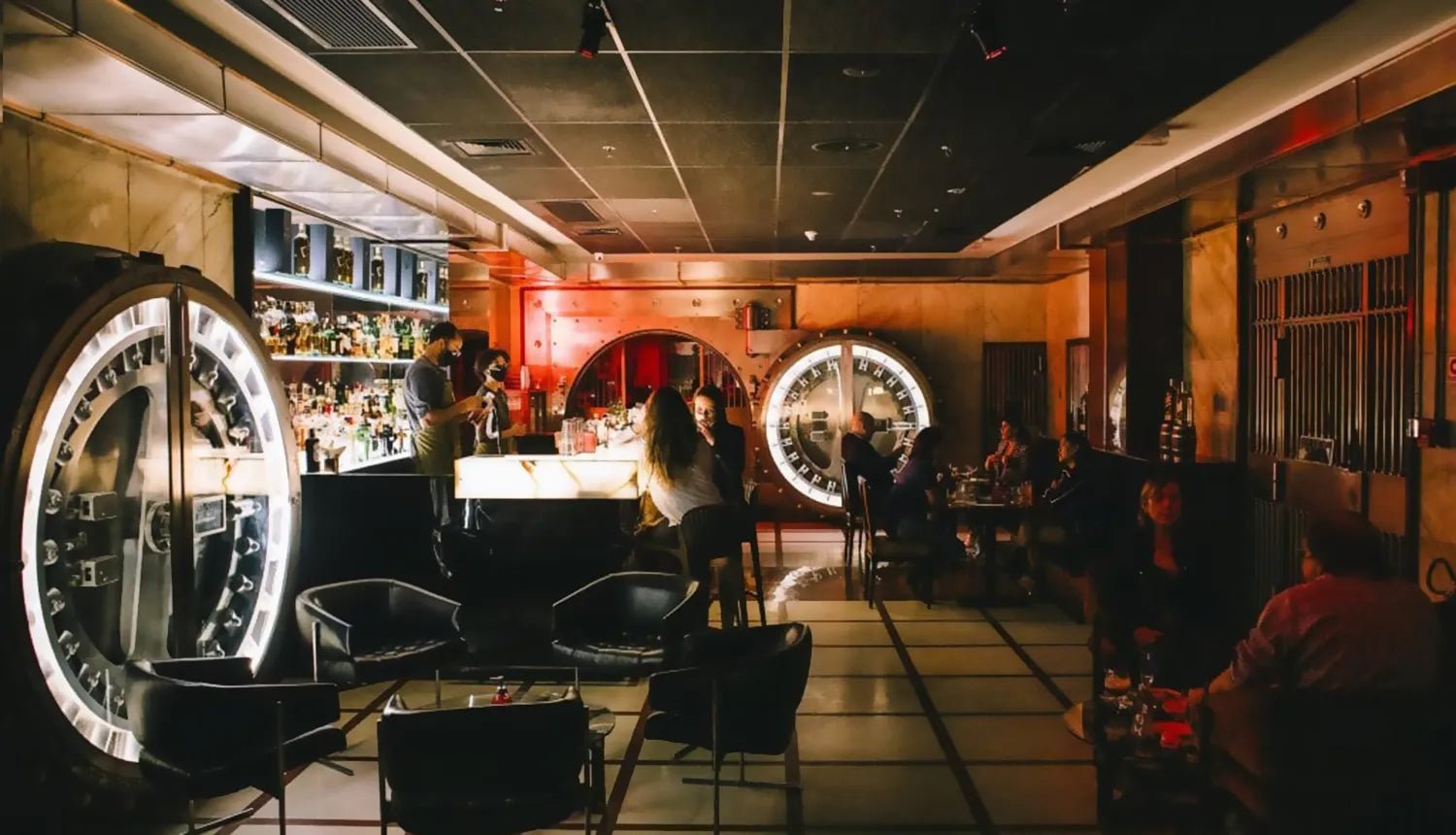 5 lugares para curtir o Dia dos Namorados - Dr. JONES. Foto em que se mostra o interior do Bar do Cofre, em São Paulo, com luzes brancas, cadeiras avermelhadas e teto e chão com cores acobreadas.