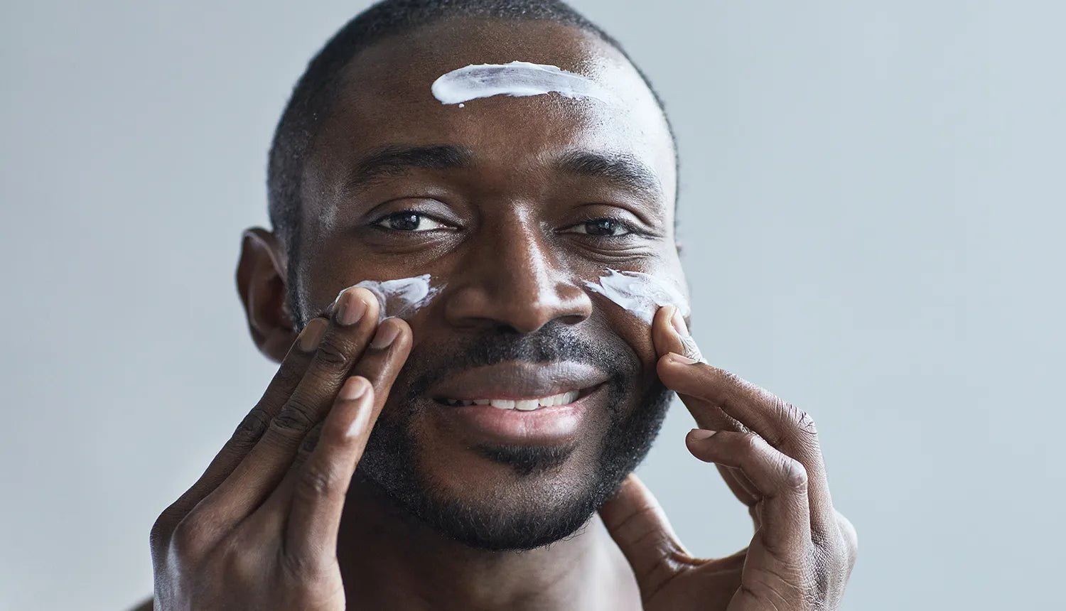5 dicas de cuidados com a pele no inverno - Dr. JONES. Foto de homem negro, barba curta, cabelo raspado, passando cremes na testa e nas bochechas.