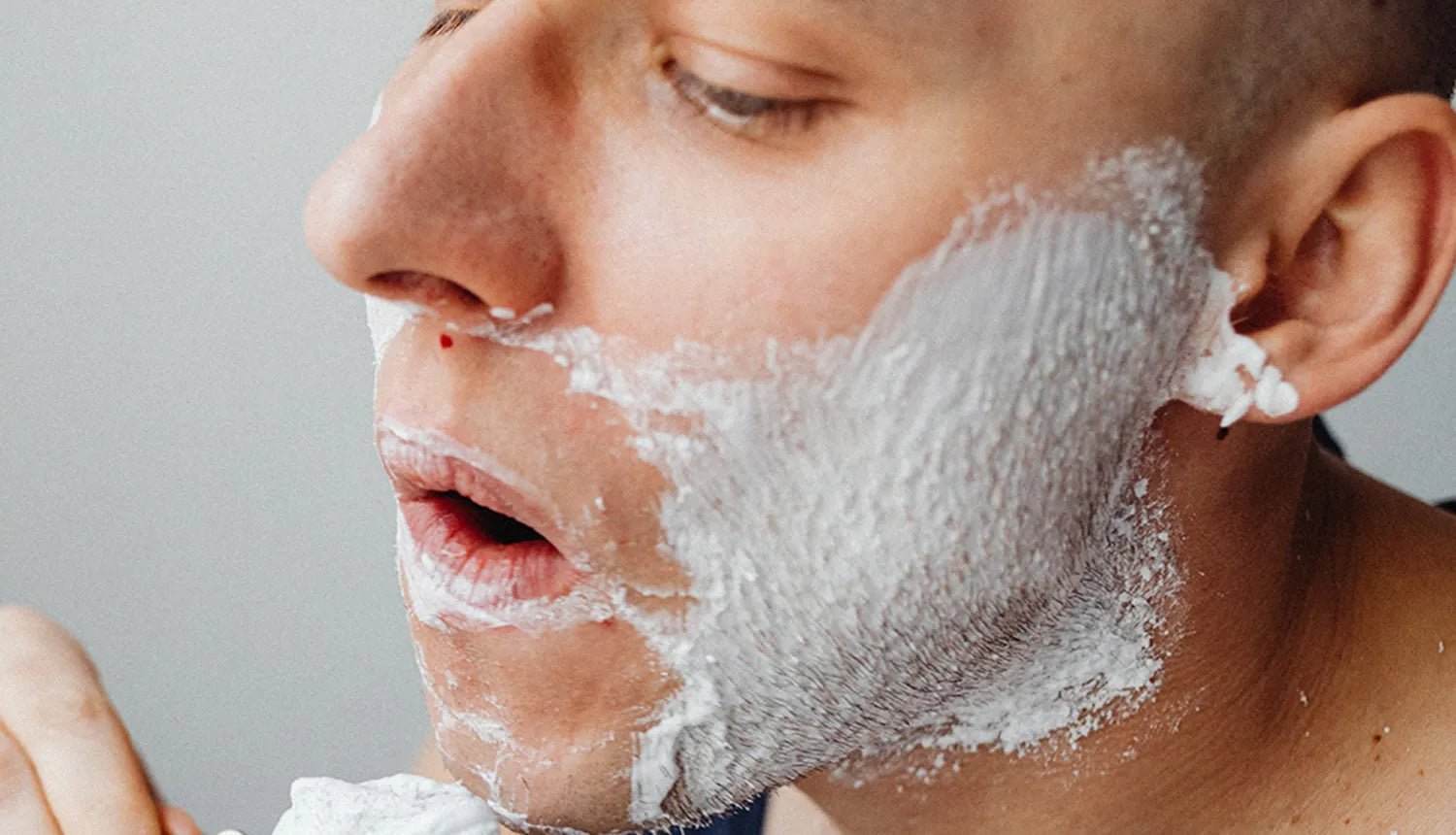 4 erros que os homens cometem na hora de fazer a barba - Dr. JONES. Foto de homem de cabelo raspado e pele clara com creme de barbear e um pequeno corte próximo ao nariz.